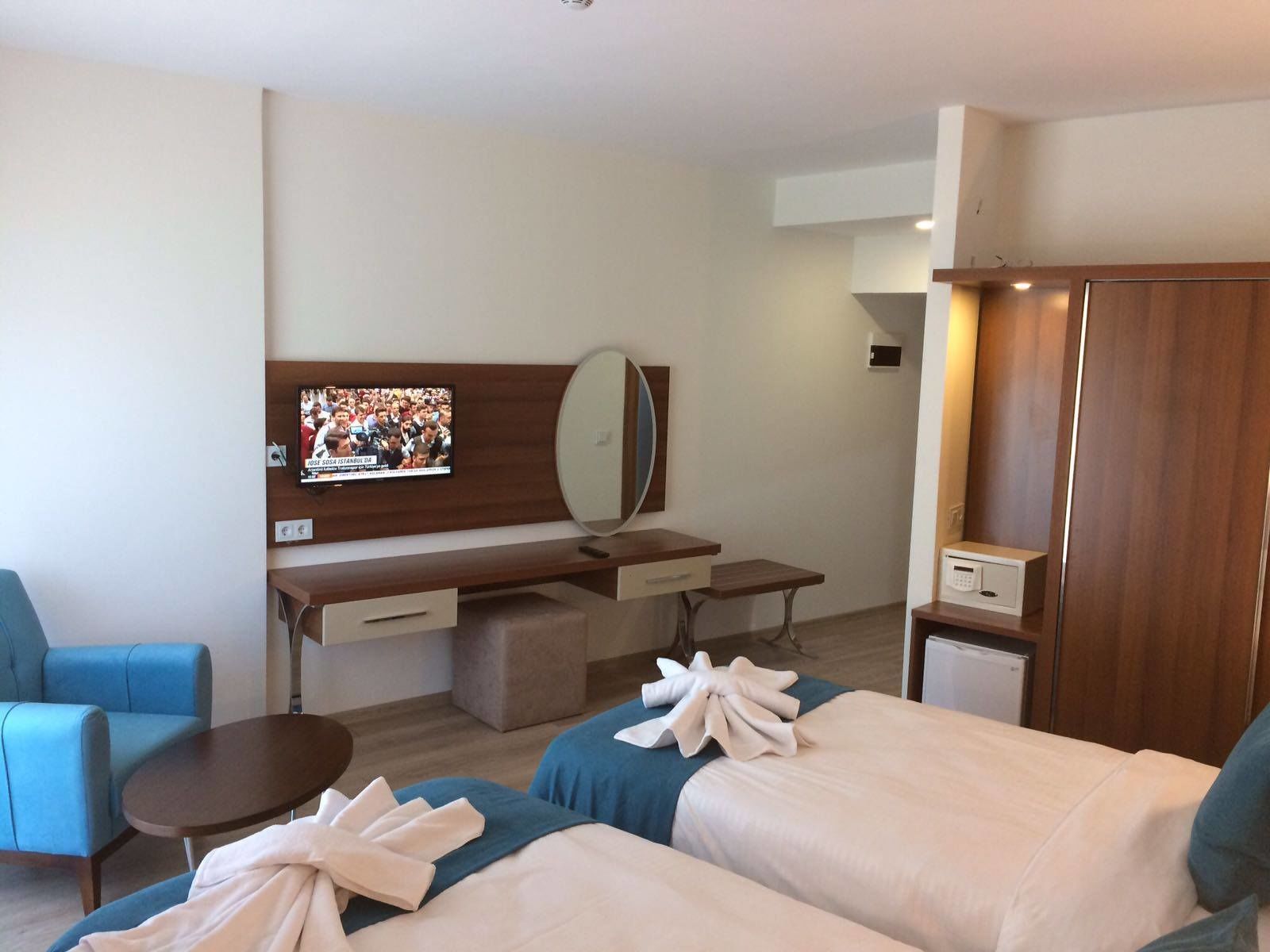 A hotel room with two beds, a desk with a TV, a mirror, a wardrobe, and a small table.