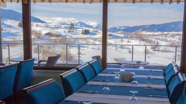 Un restaurante con vistas a montañas nevadas. Las mesas están dispuestas con sillas azules y manteles blancos.