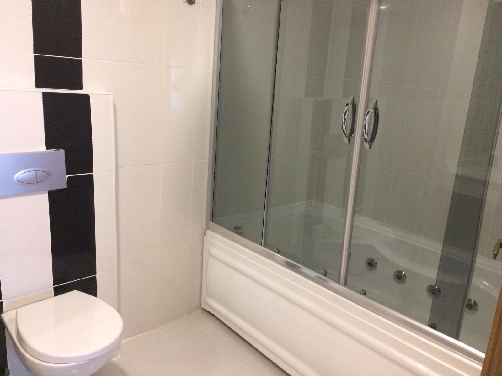 A bathroom with a white toilet, a glass-enclosed shower, and black and white tiled walls.