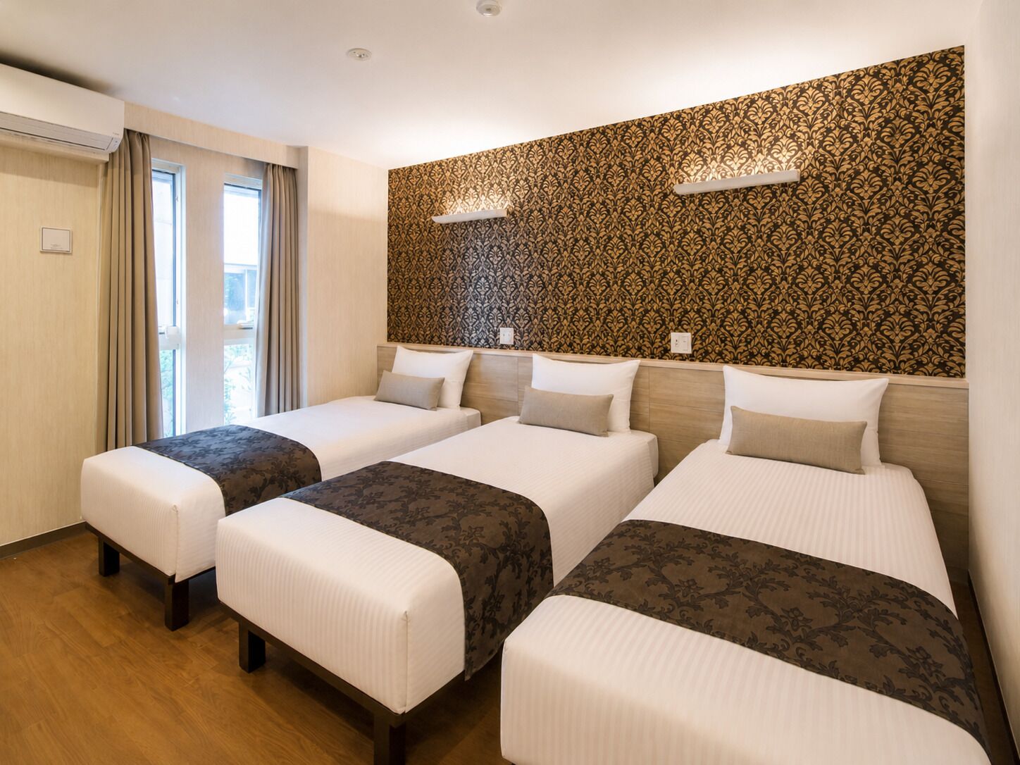 A hotel room with three beds, a large window with curtains, and a patterned wall.