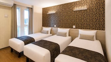 A hotel room with three beds, a large window with curtains, and a patterned wall.