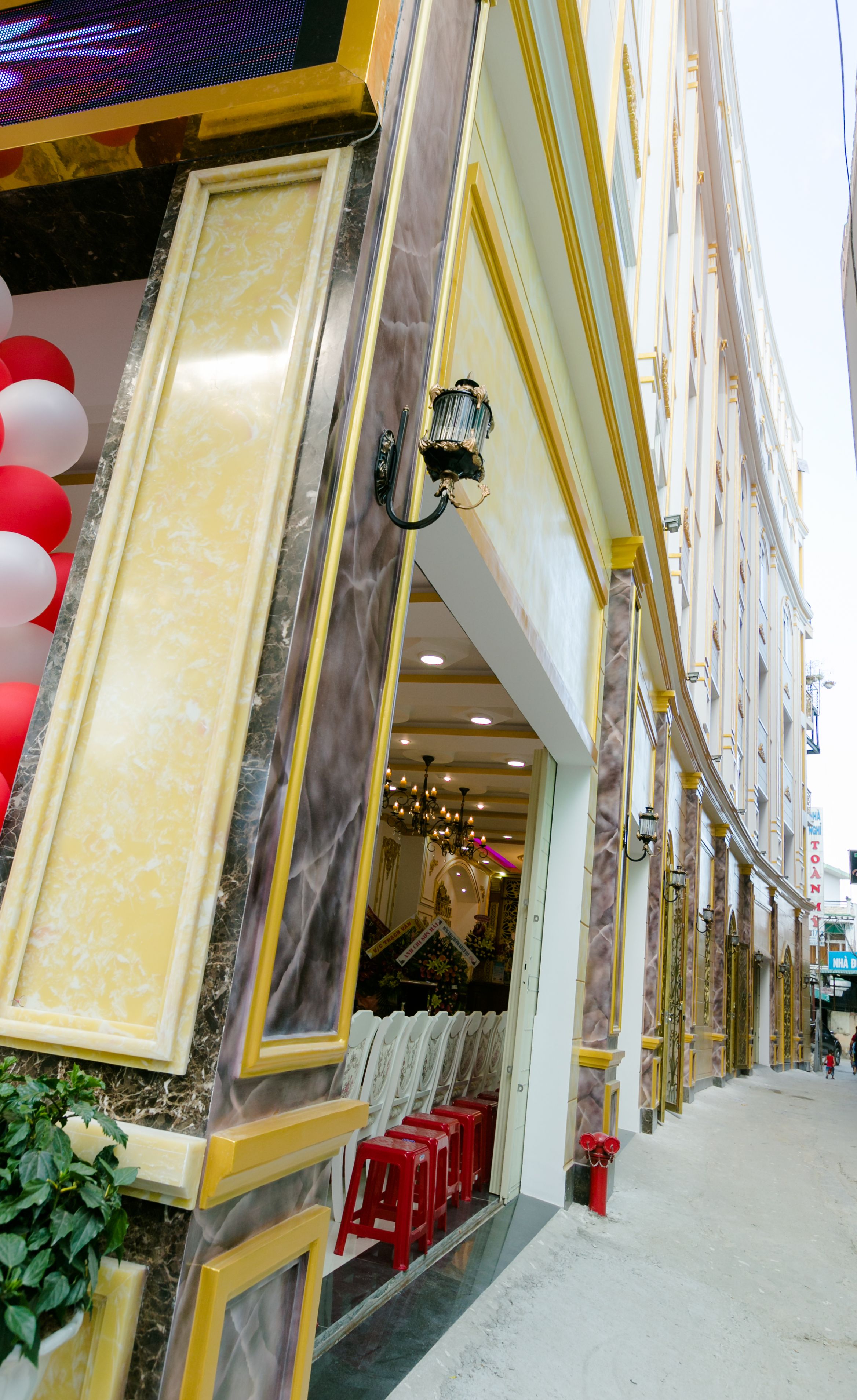 A building facade with a grand entrance, a chandelier, and red stools outside.