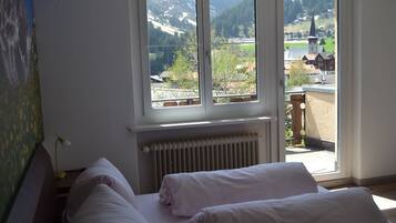 A bedroom with two beds, a radiator, and a window with a view of a village and mountains.