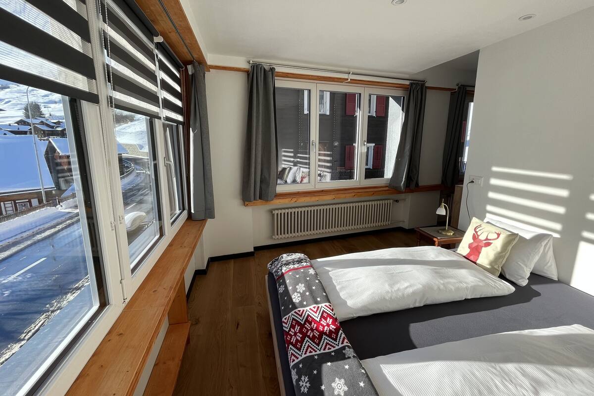 A hotel room with a large window, a bed, a nightstand, and a view of the outside.