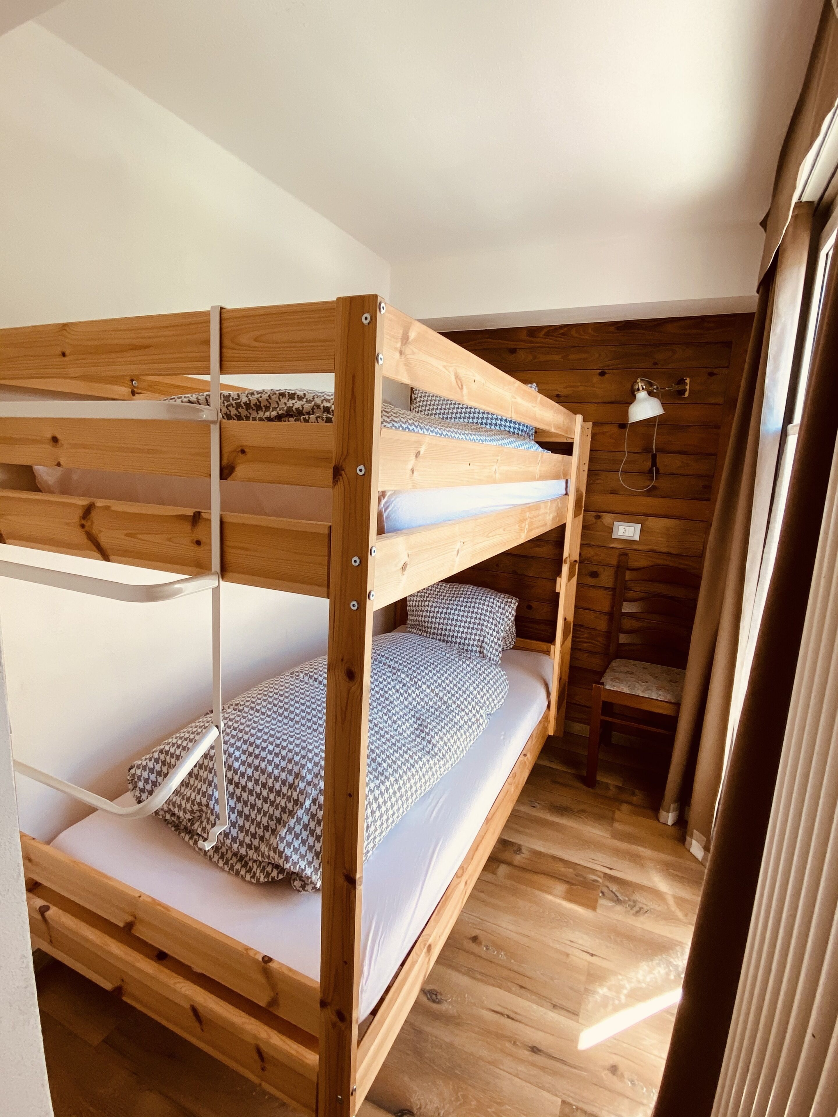 A bunk bed with wooden construction, white bedding, and a small bedside table with a lamp.