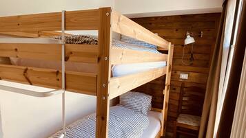 A bunk bed with wooden construction, white bedding, and a small bedside table with a lamp.