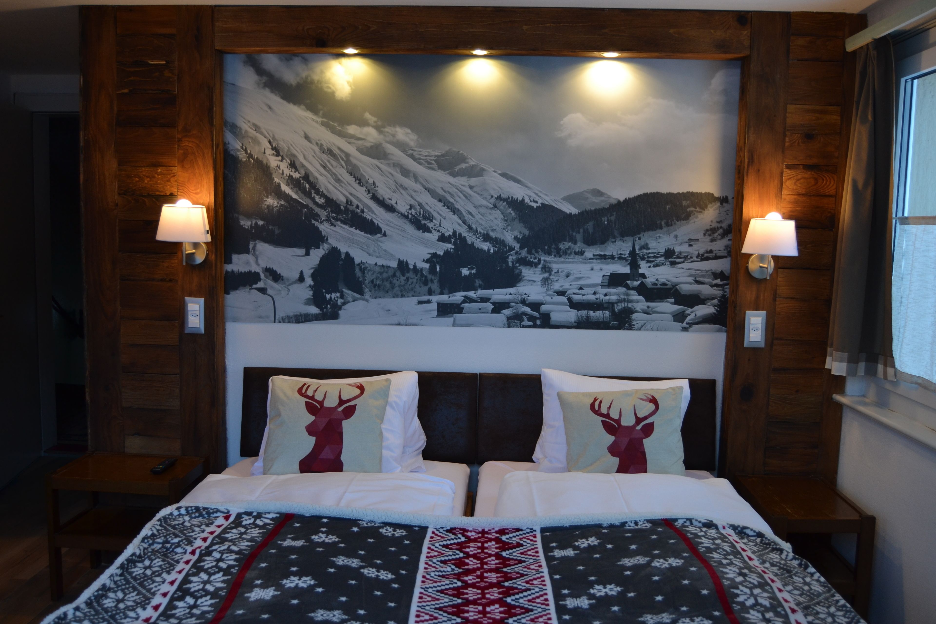 Un lit double avec une couvre-lit à motifs, deux oreillers décorés de motifs de rennes et un tableau représentant un paysage de montagne enneigé, accroché au mur.