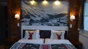 Un lit double avec une couvre-lit à motifs, deux oreillers décorés de motifs de rennes et un tableau représentant un paysage de montagne enneigé, accroché au mur.