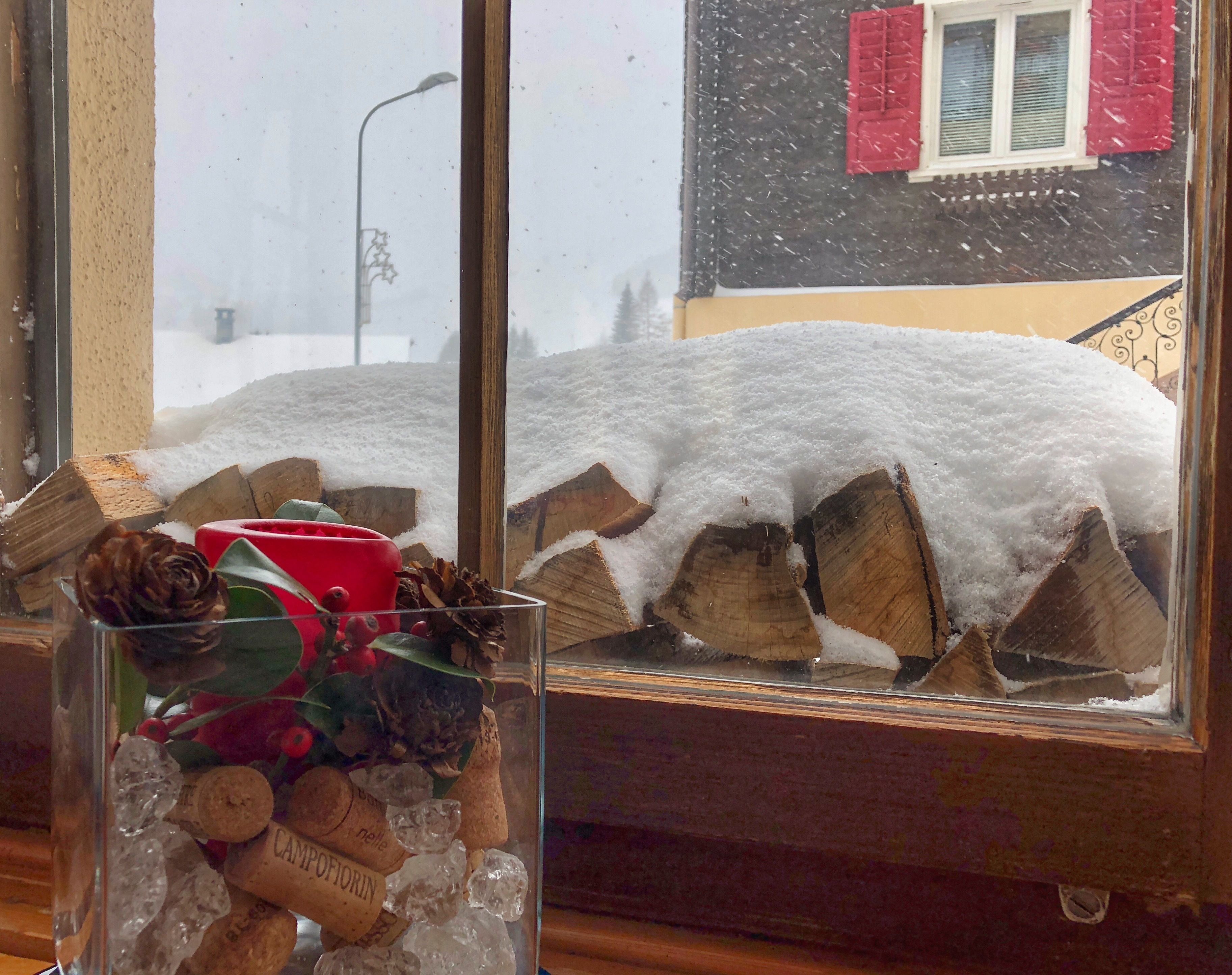 Una finestra amb vista a un paisatge nevado, un vas de vidre amb objectes decoratius i un tronc de fusta cobert de neu.
