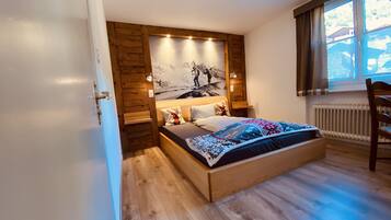 A bedroom with a wooden bed, a nightstand, a wall-mounted light, and a window with curtains.