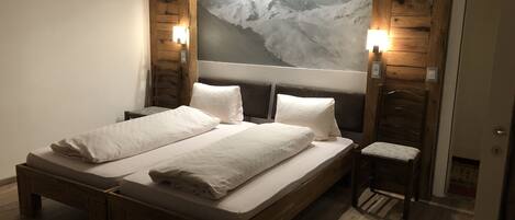 A double bed with a wooden frame and two bedside tables, each with a wall-mounted light. A large framed picture of a snowy mountain is above the bed.
