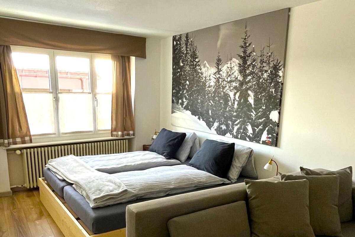 A bedroom with a bed, a sofa, a radiator, and a window with curtains.