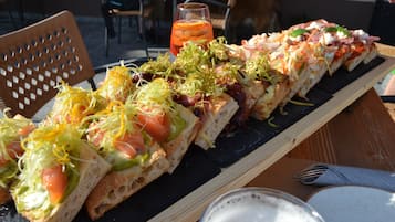 A wooden table with a black slate serving board holding a variety of open-faced sandwiches and a glass of iced tea.