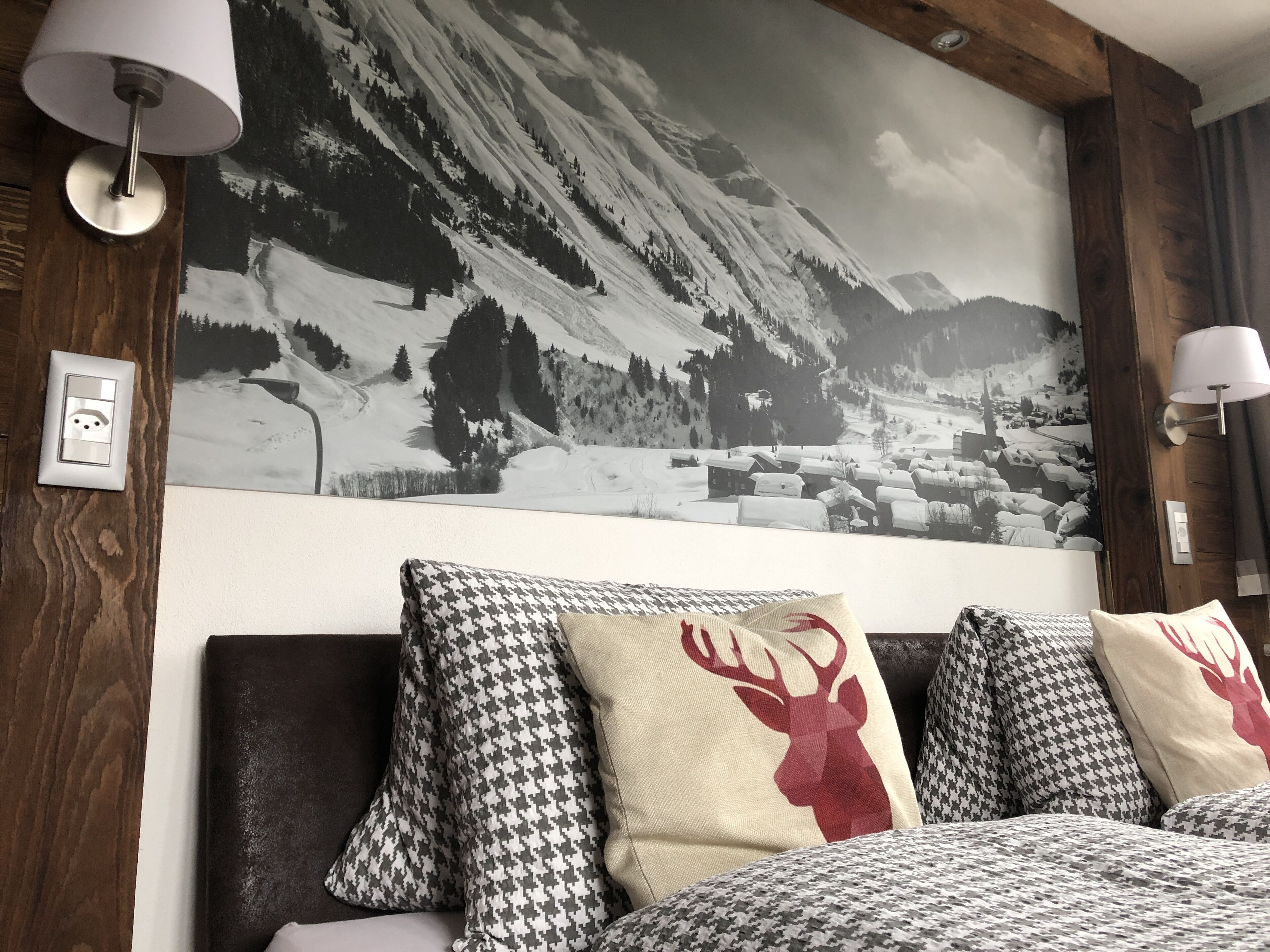 Une chambre à coucher avec une grande fresque murale représentant un paysage de montagne, des poutres en bois et des coussins à motifs.
