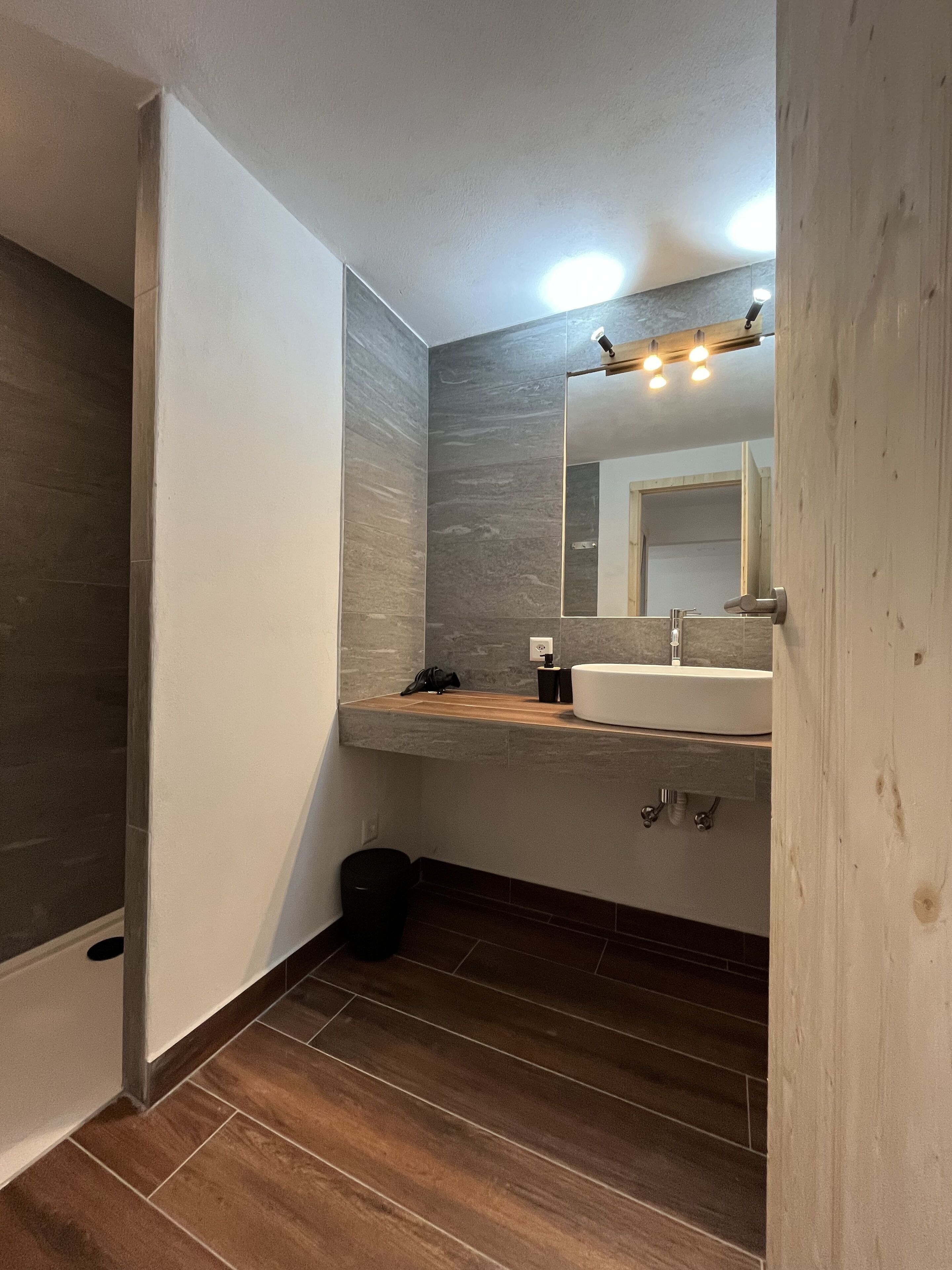 A bathroom with a wooden vanity, a white sink, a mirror, and a light fixture above the mirror.