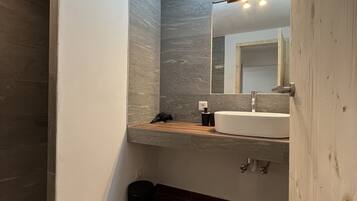 A bathroom with a wooden vanity, a white sink, a mirror, and a light fixture above the mirror.