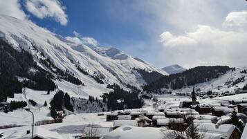 Un village enneigé, avec ses maisons traditionnelles en bois, une église et des montagnes en arrière-plan.