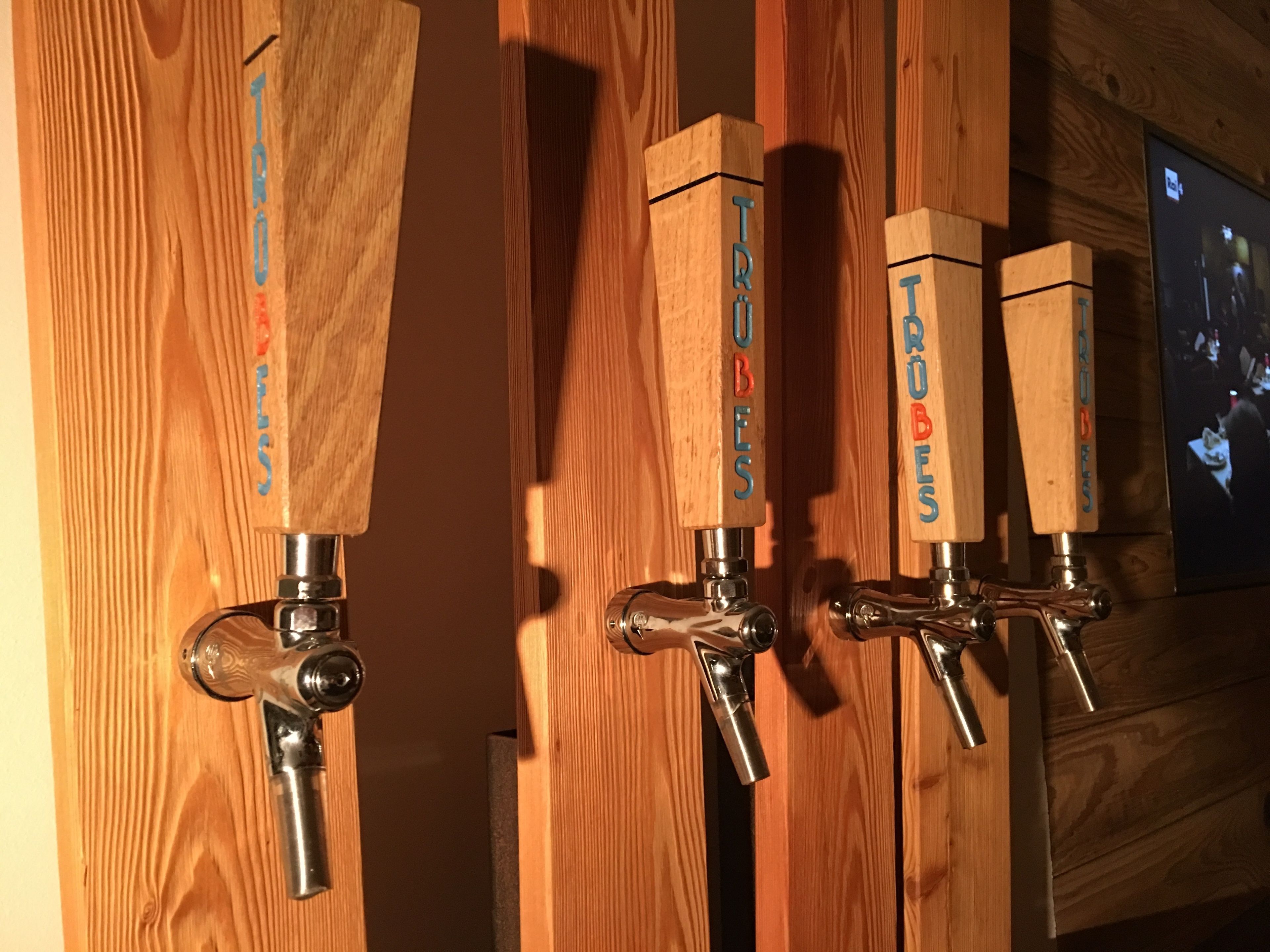 A row of wooden beer taps labeled "TRÖBELS" mounted on a wall with a wooden panel background.