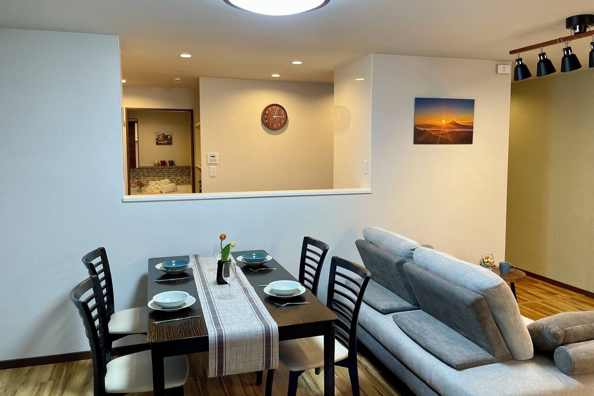 Een eethoek met een tafel voor vier personen, een bank en een klok aan de muur.