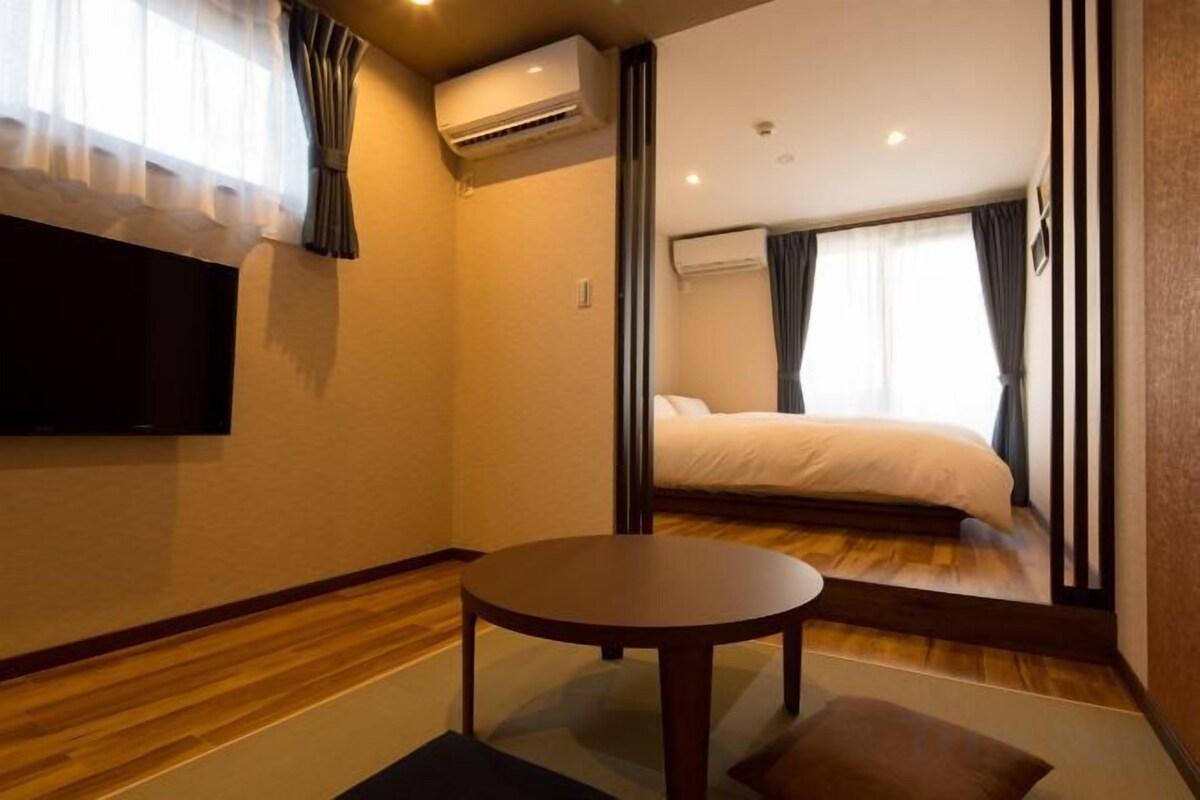 A hotel room with a bed, a round table, and a TV mounted on the wall.