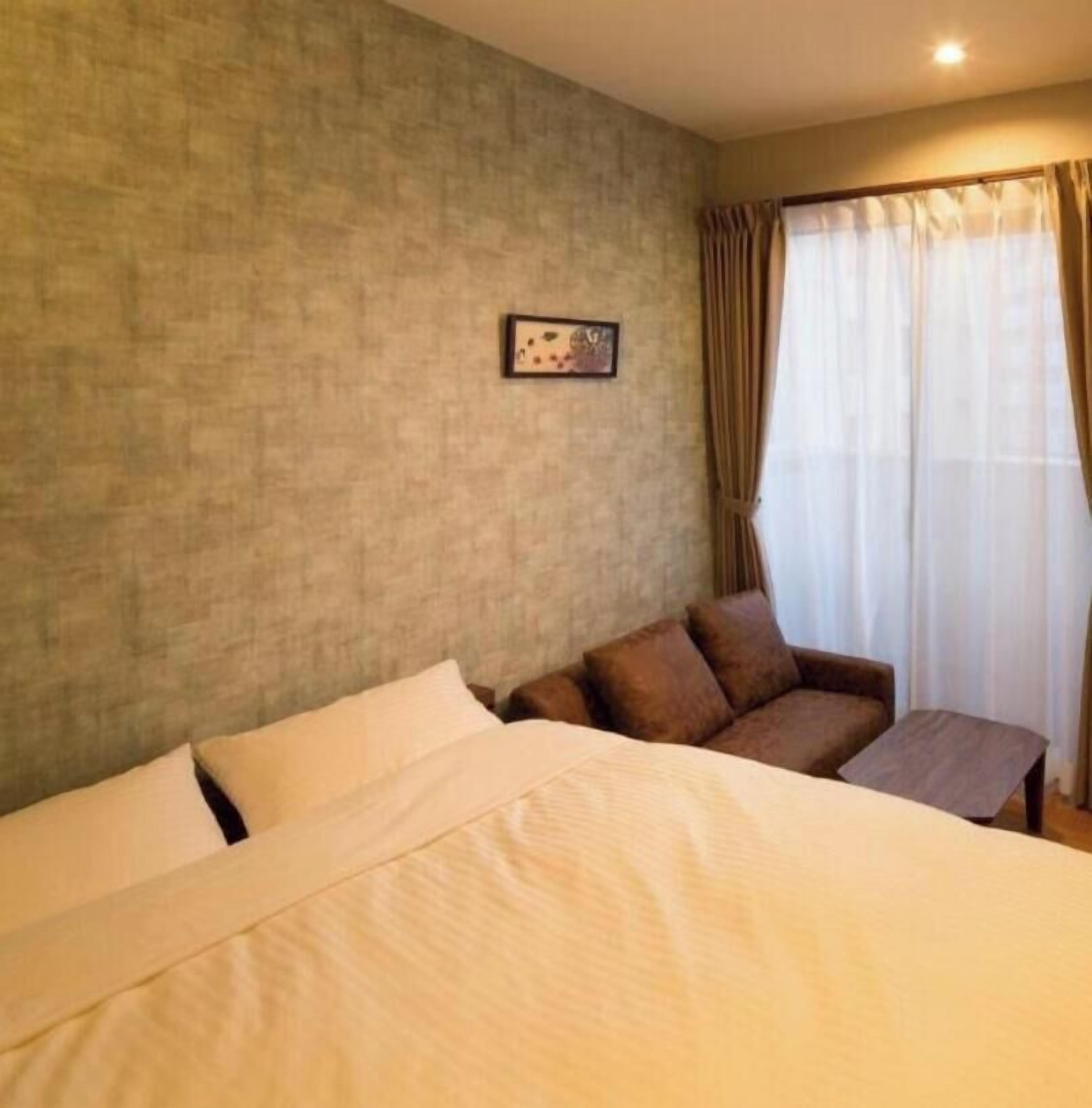 A hotel room with a bed, a small sofa, a picture on the wall, and a window with curtains.