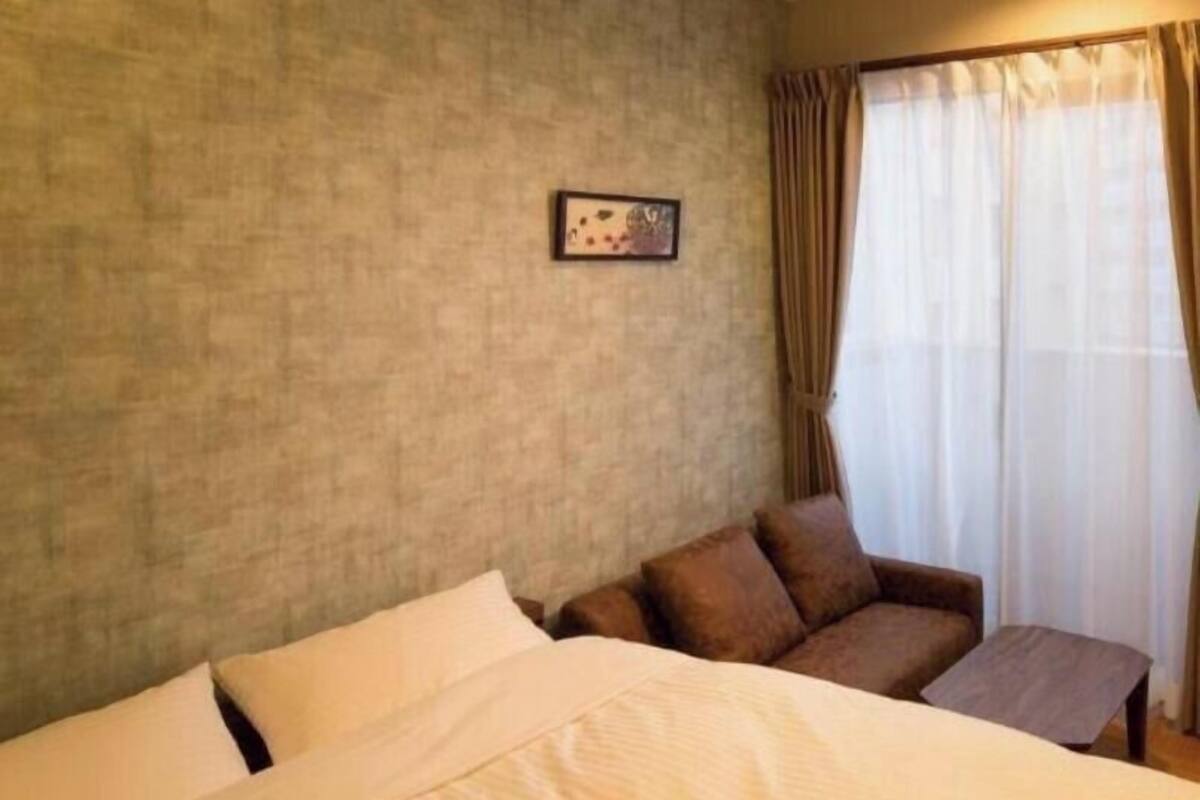 Una habitación de hotel con una cama, un pequeño sofá, un cuadro en la pared y una ventana con cortinas.