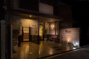 L’entrée d’un restaurant japonais traditionnel, avec une façade en bois, une enseigne et un pot de fleurs.