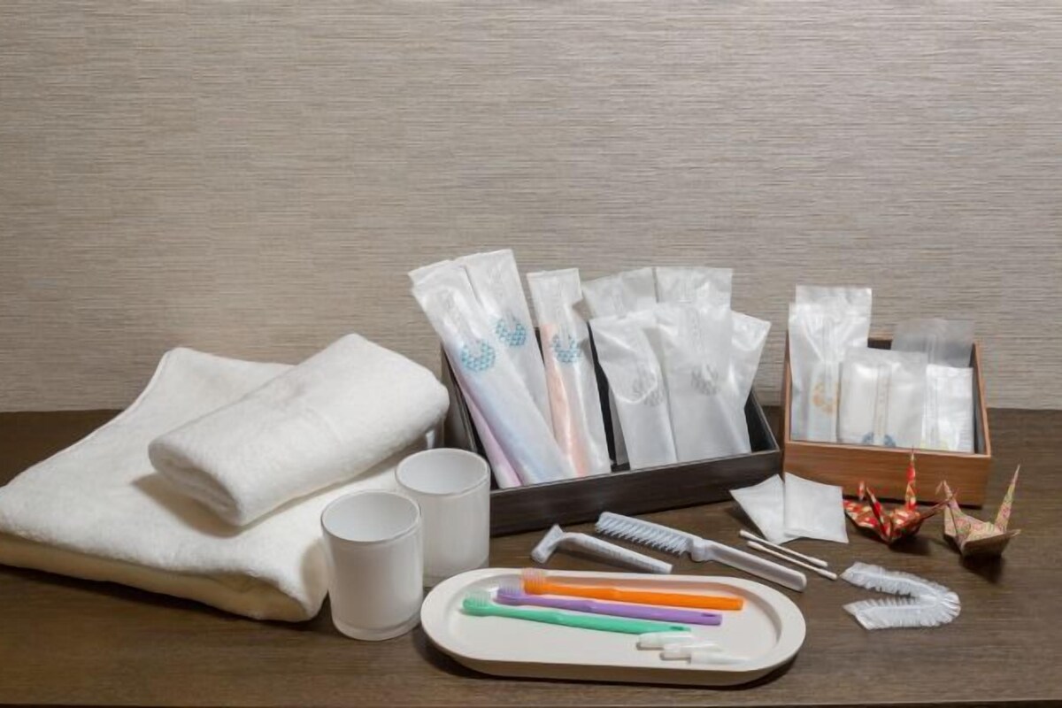 Une chambre d’hôtel bien rangée, avec une table en bois sur laquelle sont disposés des articles de toilette, une serviette blanche pliée, deux tasses blanches et un plateau contenant des brosses à dents et un peigne.
