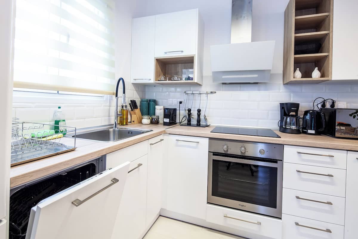 A modern kitchen with white cabinetry, a stainless steel oven, a dishwasher, and a coffee maker.