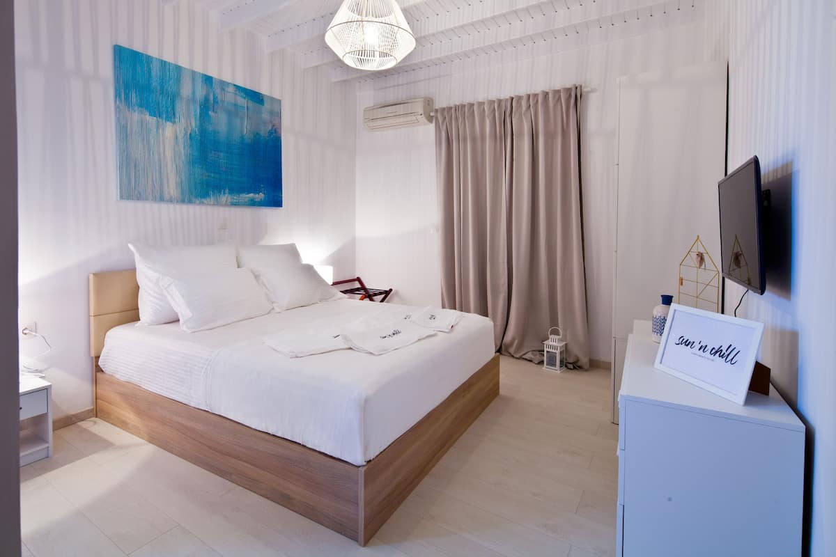 A modern bedroom with a wooden bed, a large abstract painting, a television, and a sign that reads "sun n chill".