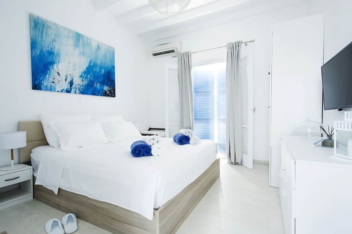 A modern hotel room with a large bed, a flat-screen TV, a desk with a computer, and a large abstract painting on the wall.