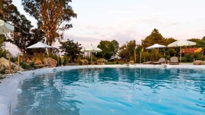 A swimming pool with lounge chairs and umbrellas, surrounded by trees and rocks.