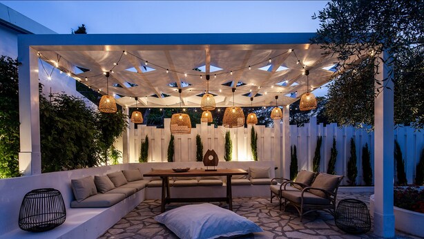 An outdoor patio with a wooden table, cushioned seating, and hanging wicker lamps.