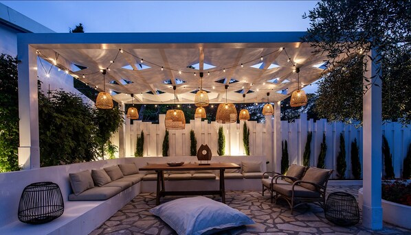 An outdoor patio with a wooden table, cushioned seating, and hanging wicker lamps.