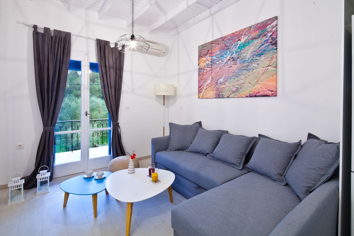 A modern living room with a blue sofa, a white coffee table, and a colorful abstract painting on the wall.