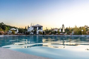 A swimming pool with lounge chairs and umbrellas, a house in the background, and a clear sky.