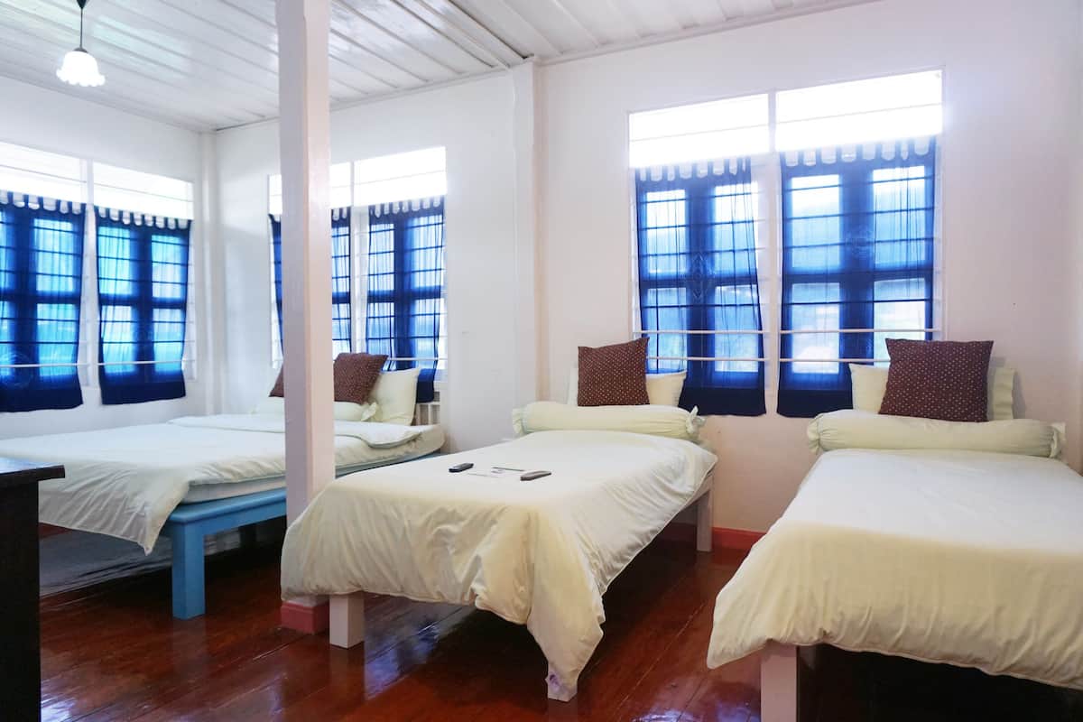 Une chambre avec trois lits, un plancher en bois et de grandes fenêtres avec des rideaux bleus.