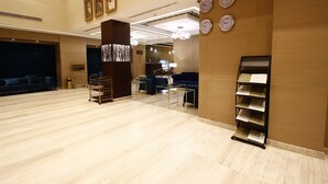 A spacious lobby with a wooden floor, a reception desk, a seating area with blue sofas, and a display rack with brochures. - Diwan Residence Hotel  Alsalamah (Jeddah)