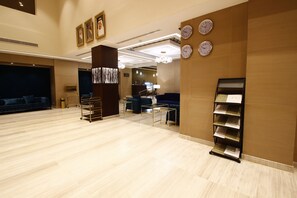 Un vestíbulo espacioso con piso de madera, una mesa de recepción, una zona de estar con sofás azules y un mostrador con folletos.
