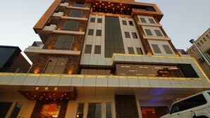 A multi-story hotel with a modern architectural design, featuring a prominent entrance with a glass facade and illuminated signage. - Diwan Residence Hotel  Alsalamah (Jeddah)