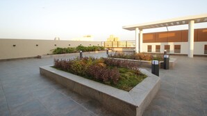 A rooftop terrace with a landscaped garden, a pergola, and a view of distant buildings. - Diwan Residence Hotel  Alsalamah (Jeddah)