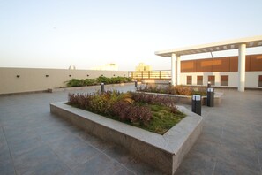 Una terraza en la azotea con jardín ajardinado, pérgola y vista a edificios distantes.