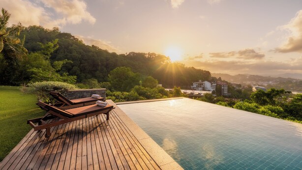 A wooden deck with lounge chairs and a swimming pool overlooking a lush green landscape and a cityscape in the distance. - Coffee Bungalow Kandy (Kandy)