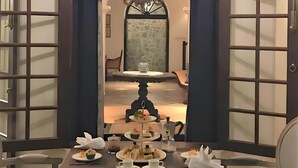 A dining area with a table set for a meal, chairs, a chandelier, and a view into a room with a stone fireplace. - Coffee Bungalow Kandy (Kandy)