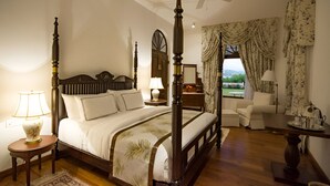 A four-poster bed with a wooden headboard, a bedside table with a lamp, and a view of the outdoors through a window with curtains. - Coffee Bungalow Kandy (Kandy)