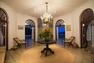 Quarto com mesa redonda, duas cadeiras, um candelabro e vista para o exterior.