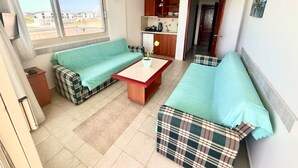 A compact living space with a sofa, a small table, and a kitchenette. - Hotel Holiday Apart (Didim)