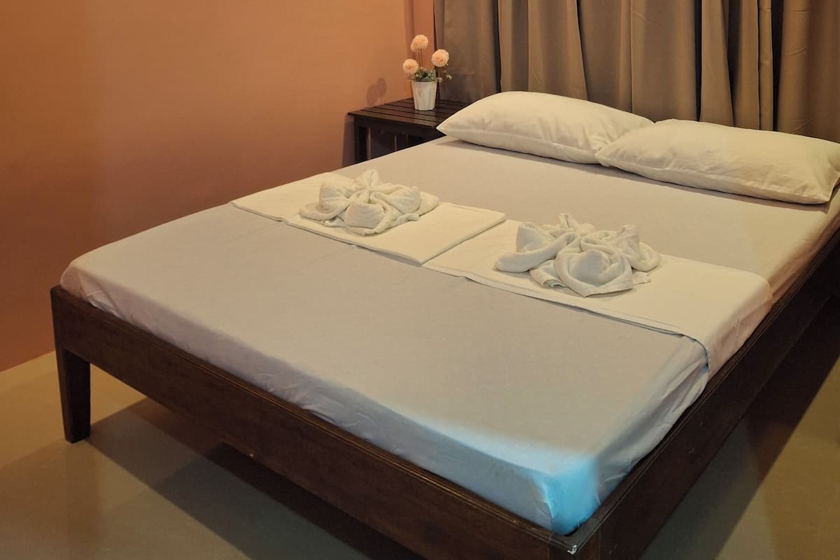 A hotel room with a bed, a nightstand, a vase with flowers, and a curtain.