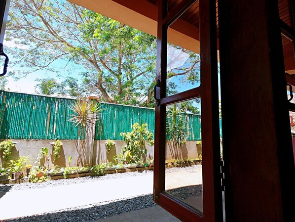 An open doorway to a room with a view of a green fence, trees, and potted plants outside. - Woodside Rogers Residence (Puerto Princesa)