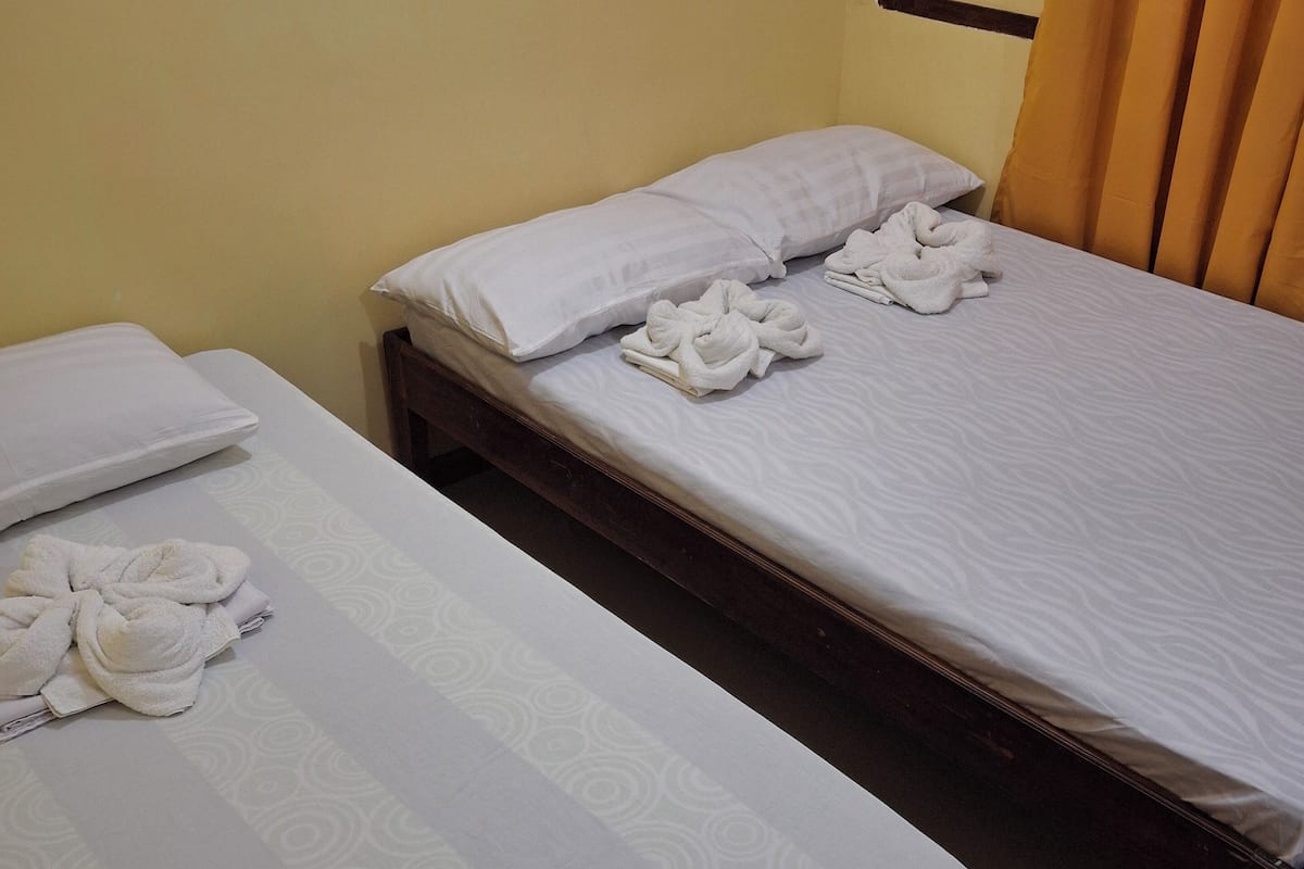 Two single beds with white linens and towels, a wooden headboard, and a yellow wall.